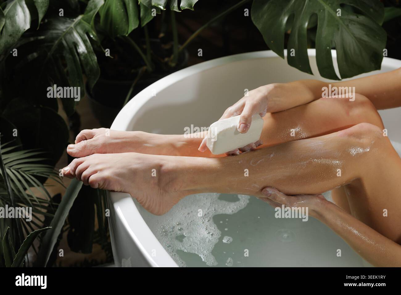 Une personne profite d'une routine de soins des pieds apaisante dans un bain luxueux entouré d'une végétation luxuriante, mettant en valeur la détente et l'auto-soin pour les amateurs de spa Banque D'Images