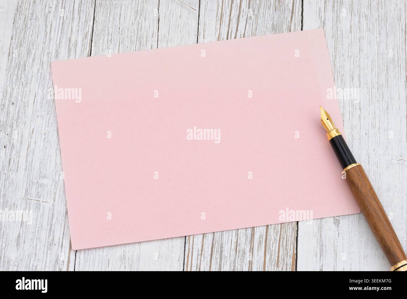 Maquette de carte vierge rose doux avec stylo plume sur le bureau en bois blanc, idéal pour la marque, l'invitation, la papeterie et la conception de message Banque D'Images