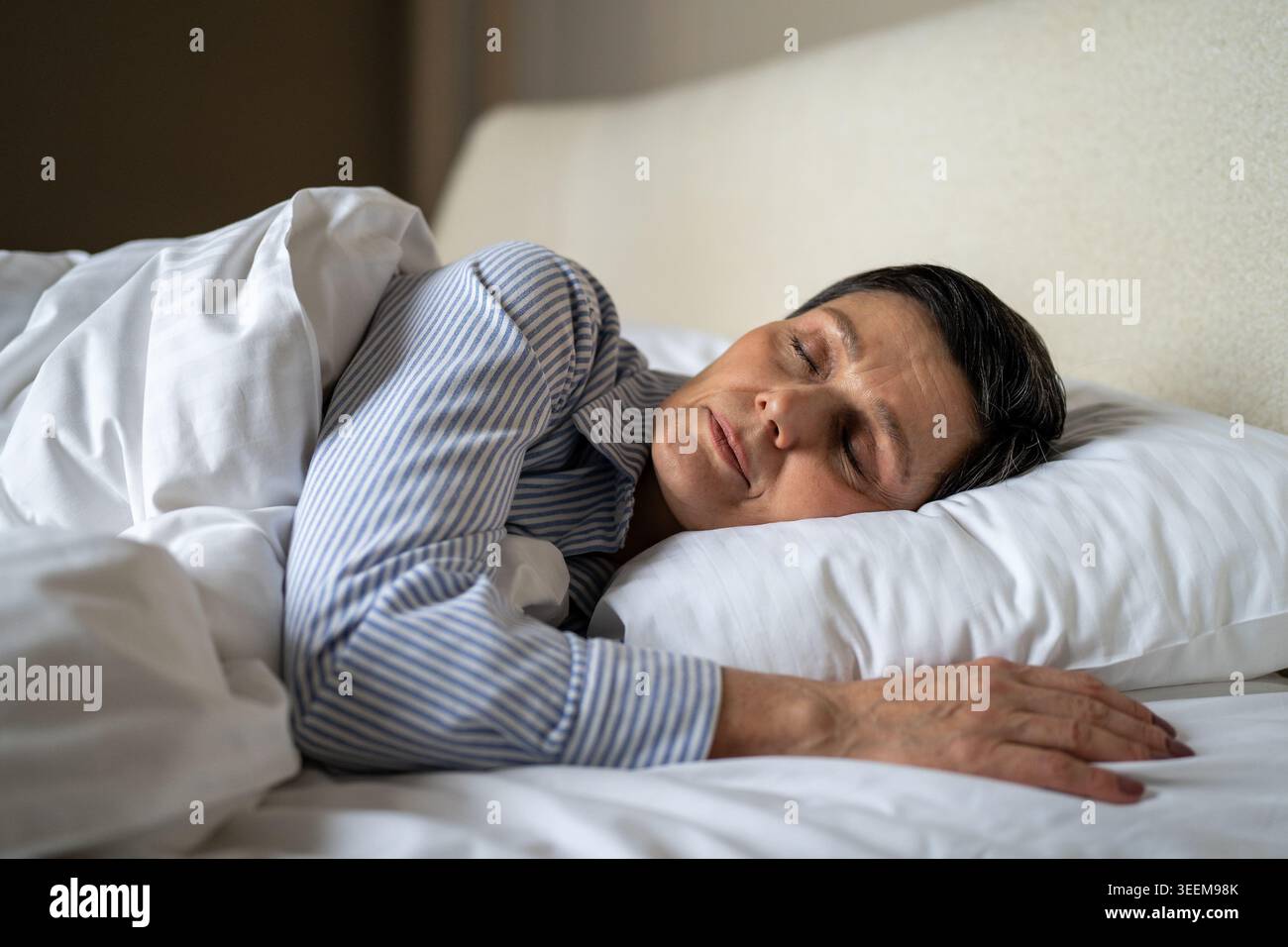 Femme senior tranquille confortablement allongé dans le lit dans la chambre couverte de couverture confortable et dormir. Banque D'Images