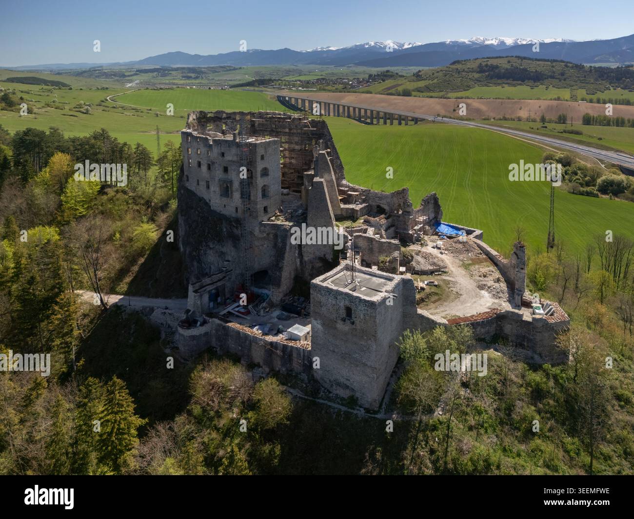 Vue aérienne des ruines médiévales du château de Likava sur une colline rocheuse entourée de champs verdoyants et de forêts avec un pont autoroutier en arrière-plan Lika Banque D'Images