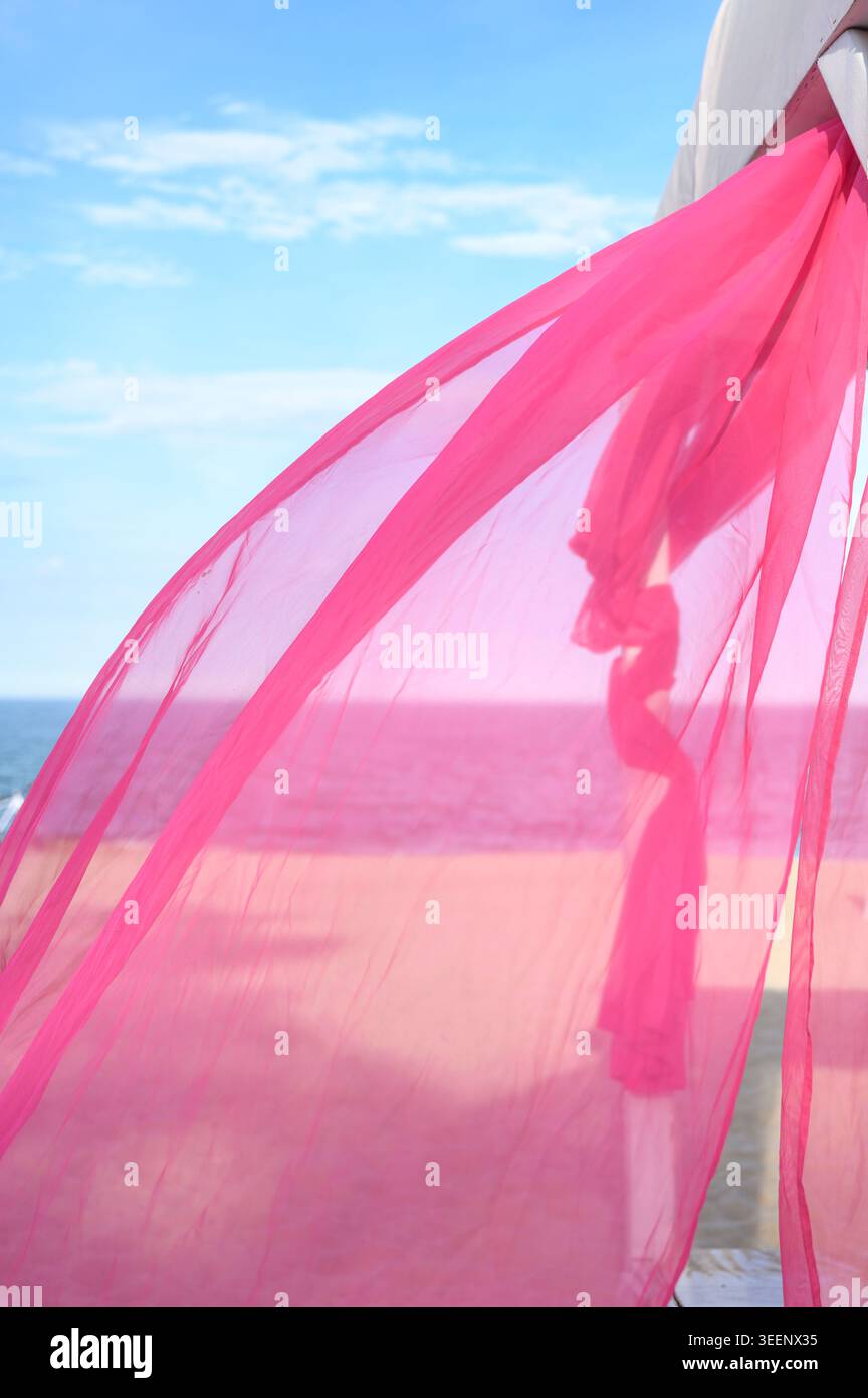 Textile rose clair soufflant dans le vent contre un horizon maritime. Des ondulations douces atteignent le sable. Concept de vacances esthétiques et de beauté naturelle Banque D'Images
