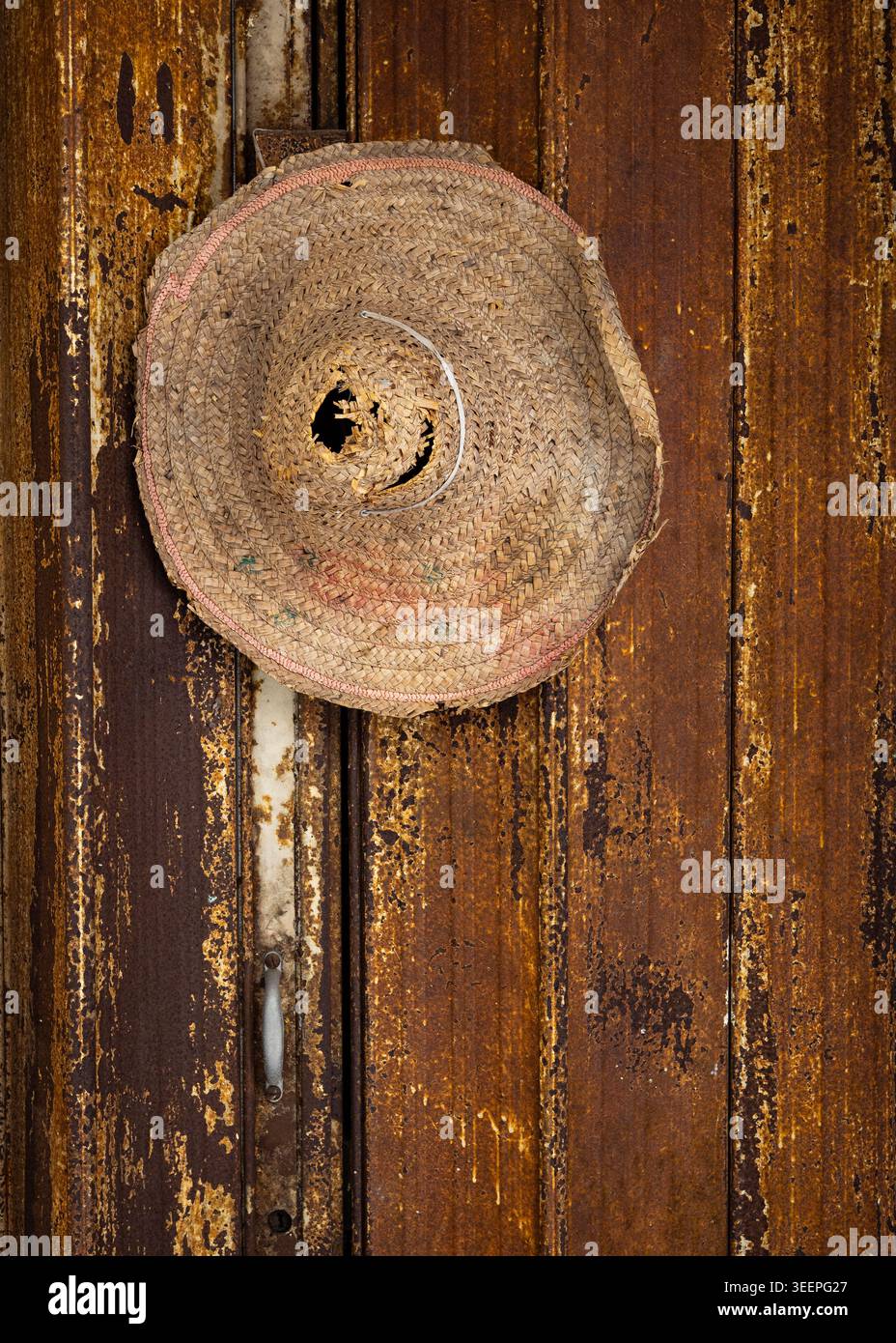 Détail en gros plan d'un chapeau rustique de travailleurs de paille attaché à un fond de porte rouillé., panneau altéré, Ipoh, Perak, Malaisie Banque D'Images