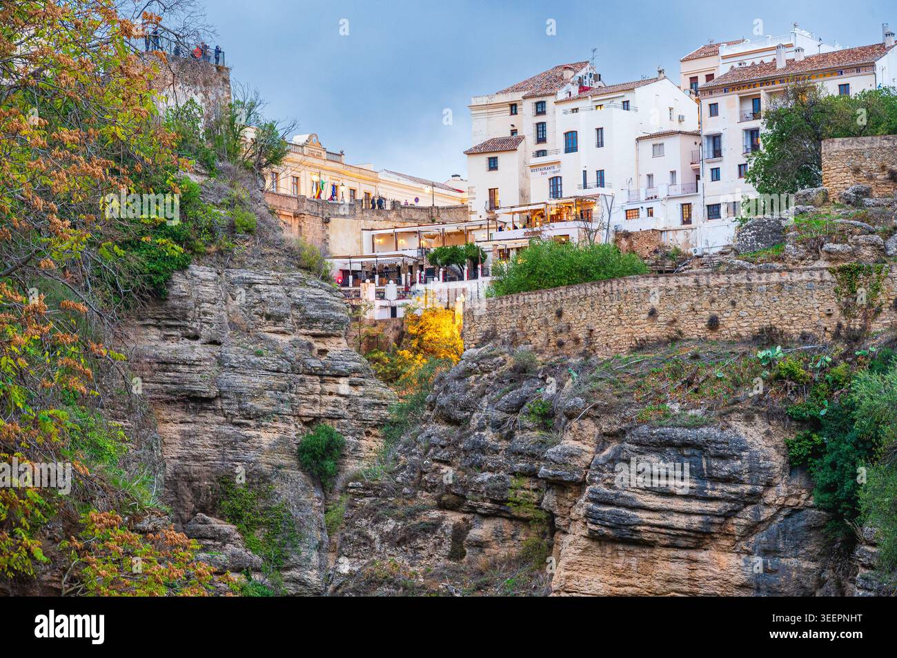 Les bâtiments blancs et les terrasses de restaurants de Ronda se dressent au bord d'une gorge rocheuse avec des murs de pierre et de la végétation en Andalousie, Espagne. Arbres et shr Banque D'Images