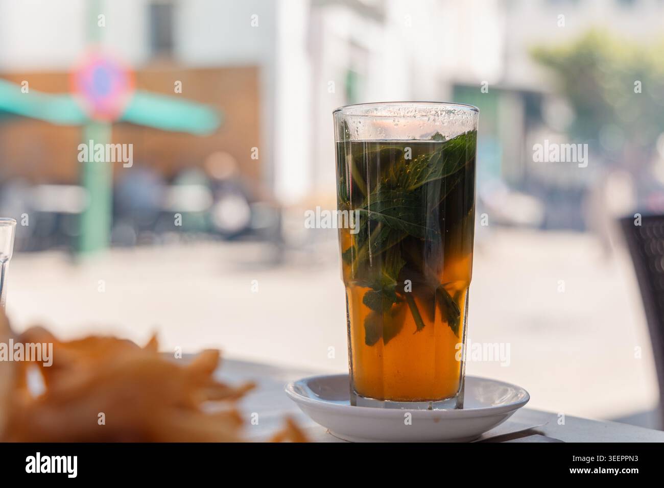 Rafraîchissant thé à la menthe marocaine avec des feuilles fraîches dans un grand verre, reposant sur une soucoupe blanche dans un café en plein air Banque D'Images