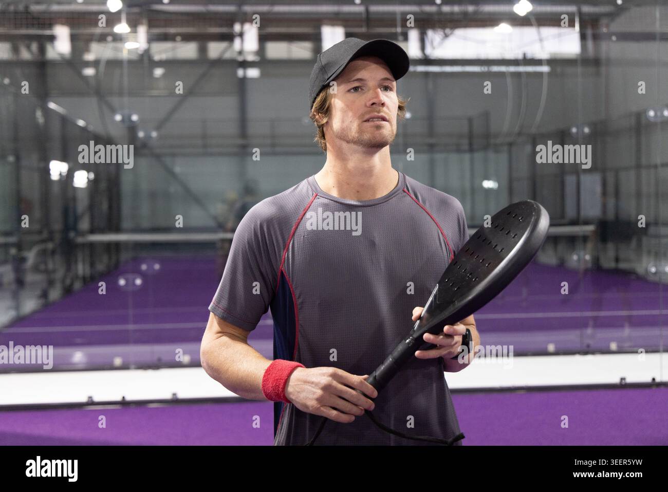 Athlète masculin tenant une pagaie perforée noire debout sur un court violet avec des panneaux de verre portant une casquette Banque D'Images