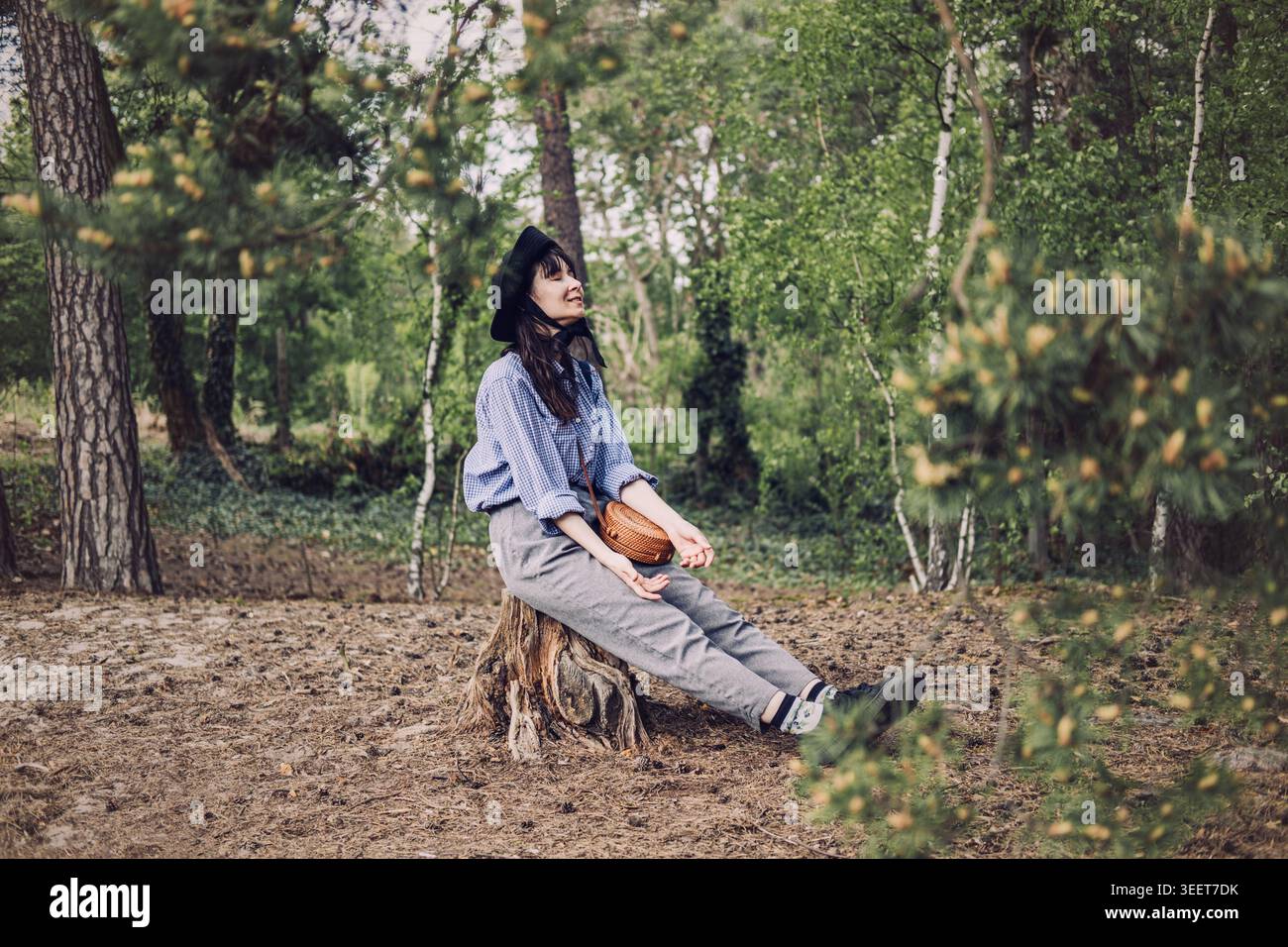 La personne portant un chapeau est assise sur la souche d'arbre dans la forêt avec les yeux fermés. Expérience de randonnée consciente, voyage de détox numérique, pratique de l'éco-thérapie. Banque D'Images