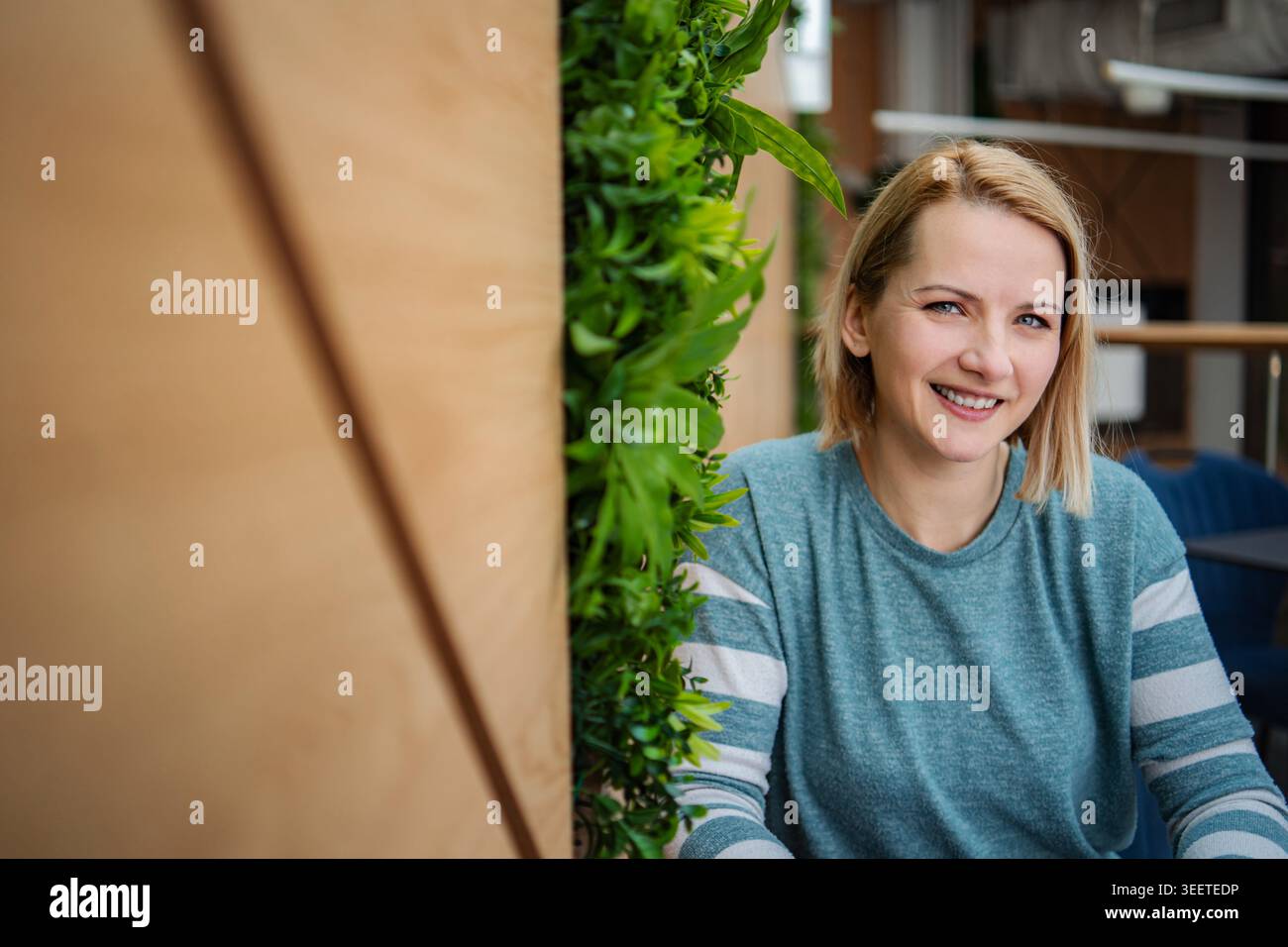 Femme blonde souriante dans un jardin vertical de bureau moderne Banque D'Images