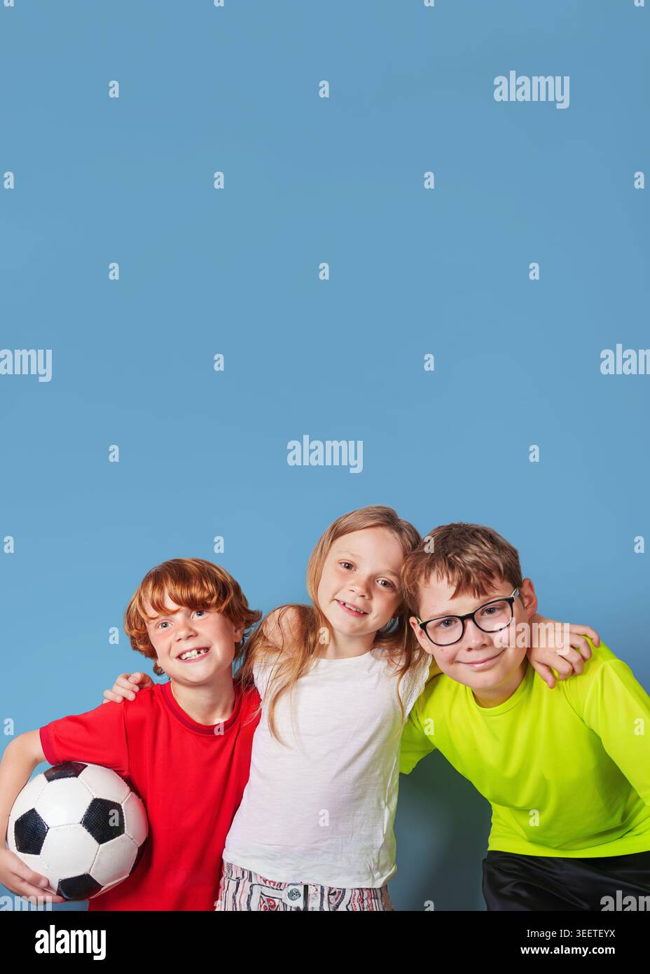 Rire les enfants avec le ballon de football s'amusent, isolés sur fond bleu. Affiche avec espace de copie. Banque D'Images