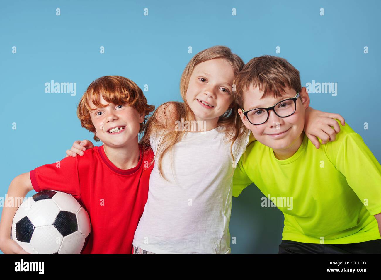 Rire les enfants avec le ballon de football s'amusent, isolés sur fond bleu. Banque D'Images