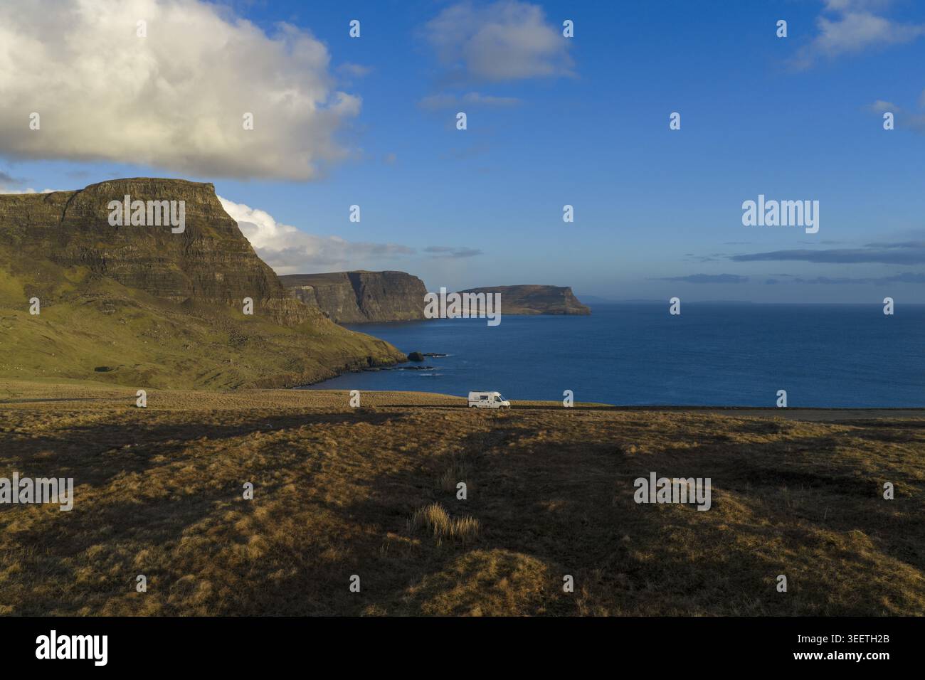 Vue aérienne d'un camping-car garé sur une route côtière surplombant les falaises spectaculaires et l'océan bleu sous un ciel lumineux à l'île de Skye. Banque D'Images