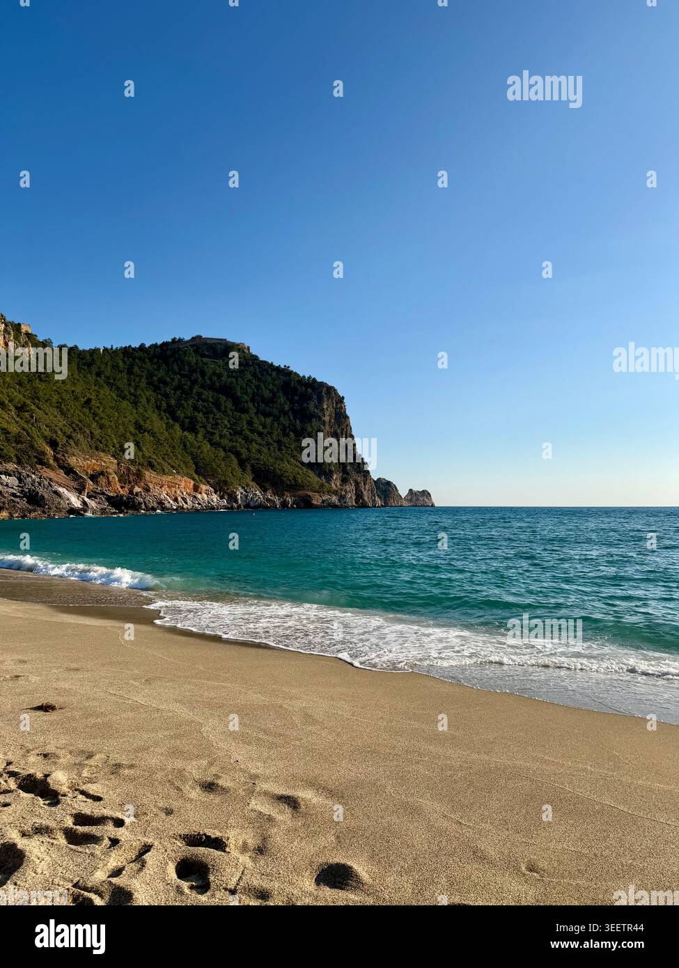 Belle plage de sable à Alanya, Turquie. Turquoise eau de mer méditerranéenne avec une falaise rocheuse, paysage côtier de jour ensoleillé, station balnéaire populaire.⁠ - Image de stock capturée avec un smartphone