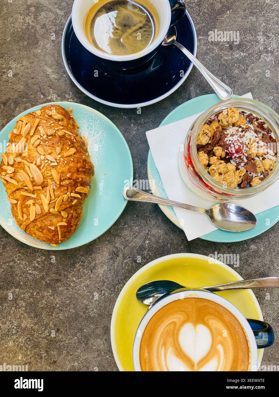 Photo à angle élevé d'un délicieux petit déjeuner : cappuccino avec Heart Latte art, café noir, croissant aux amandes et bol de yaourt granola Banque D'Images