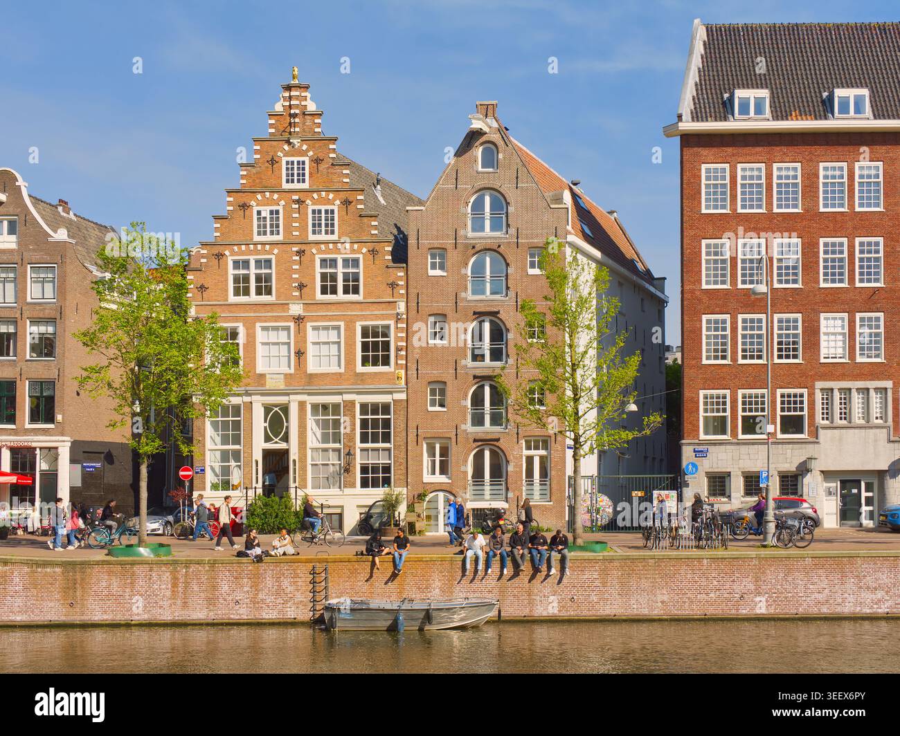 Amsterdam, pays-Bas - 29 avril 2026 : les jeunes traînent sur le canal hollandais historique le long de la voie navigable à Amsterdam avec des façades à pignon en escalier Banque D'Images