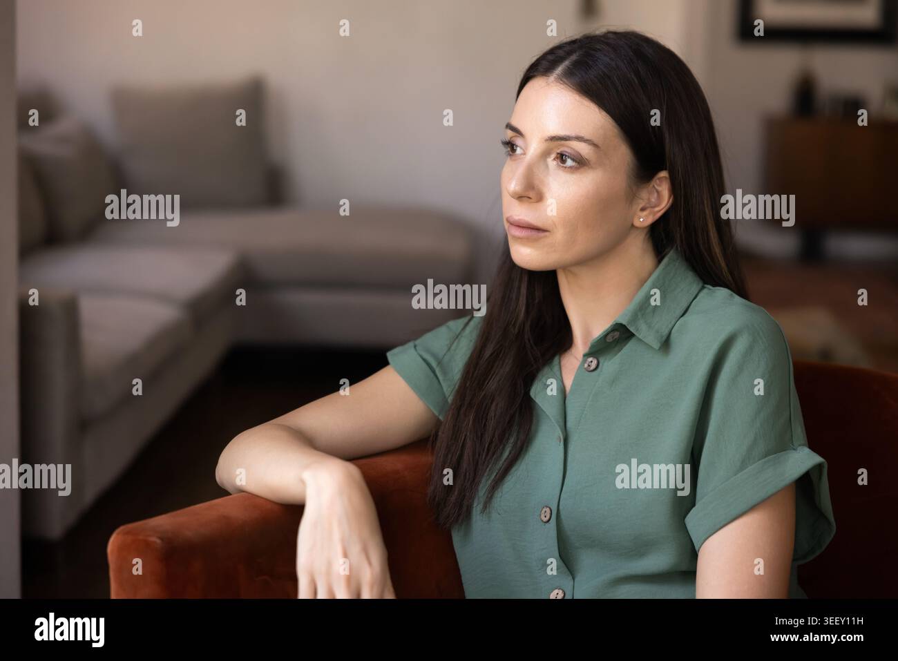 Femme pensive simple assise dans un fauteuil dans un salon moderne Banque D'Images
