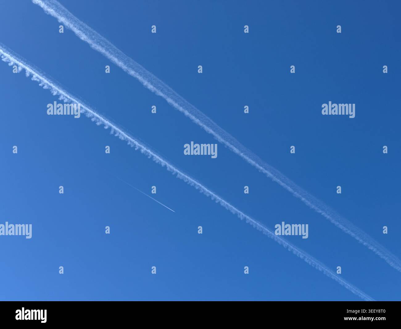 Des traînées d'avion à haute altitude créant des lignes diagonales dynamiques à travers un ciel bleu clair. Expérience minimale de l'aviation avec voyage, transport, cli Banque D'Images