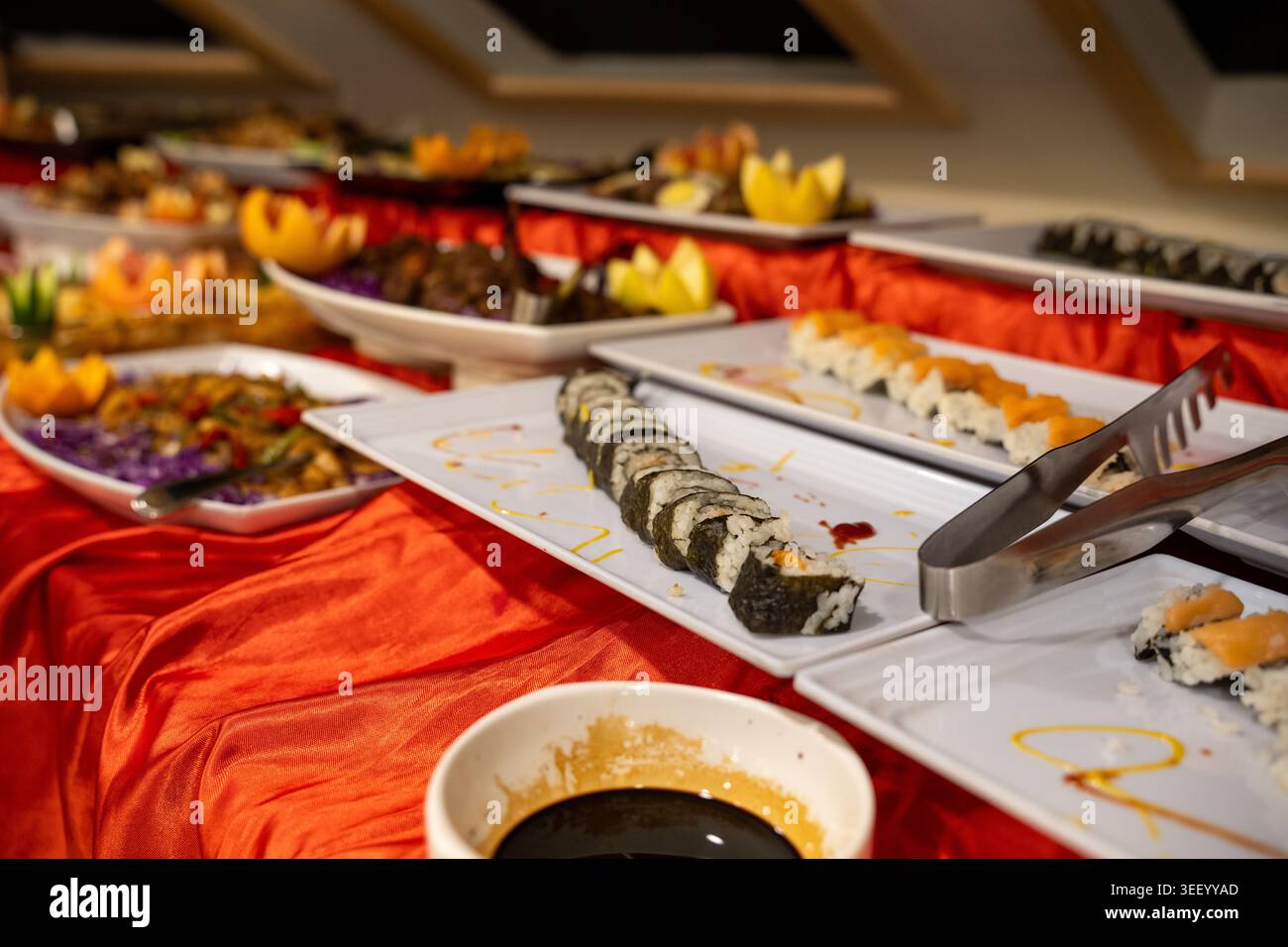 Assortiment de sushis et divers plats asiatiques disposés sur une ligne de buffet avec une nappe rouge Banque D'Images