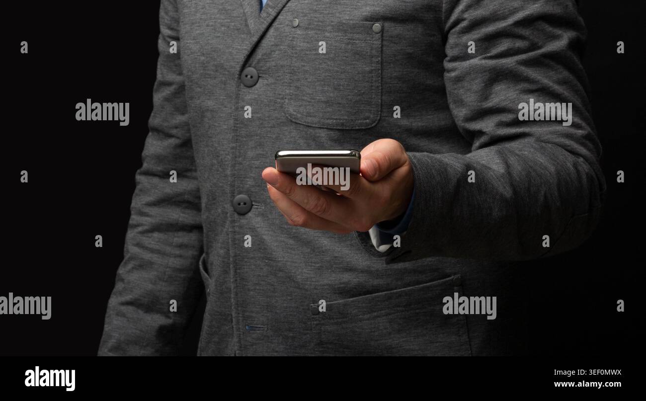 Homme en costume gris tenant smartphone sur fond sombre Banque D'Images