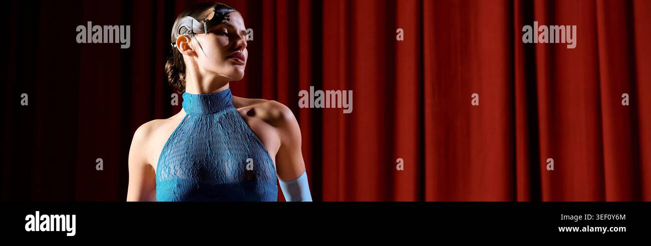 Un jeune artiste dans une tenue bleue exprime son émotion sous les lumières et les rideaux chauds de scène. Banque D'Images