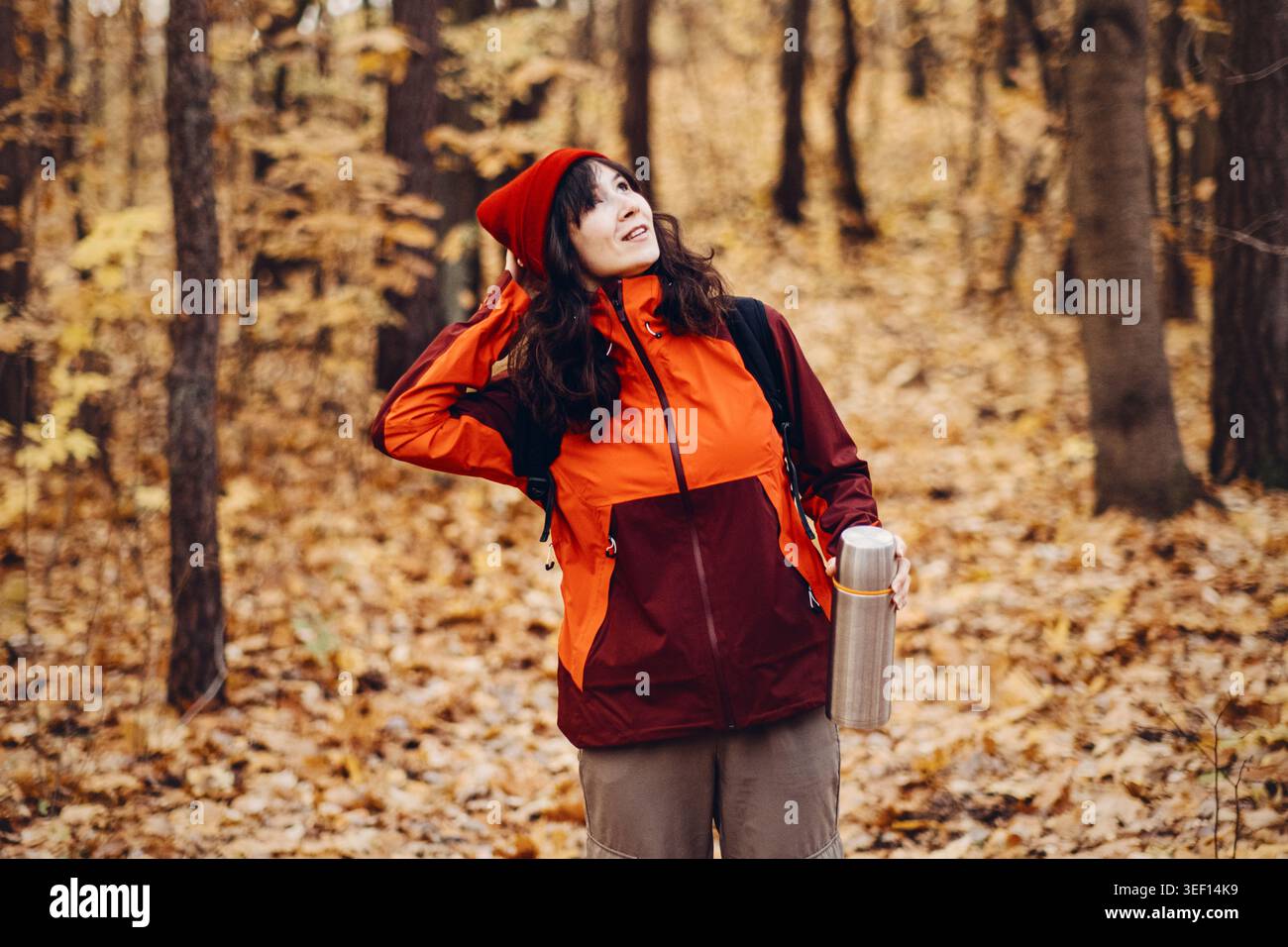 Femme se tient dans la forêt d'automne regardant vers le haut tout en tenant thermos. santé mentale en plein air, nature de soulagement du stress, forêt de bien-être psychologique, numérique Banque D'Images