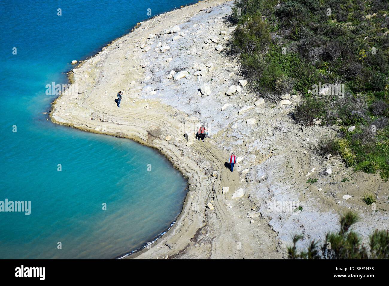 Plan en grand angle de personnes marchant le long du littoral sablonneux et incurvé d'un lac ou d'un réservoir turquoise Banque D'Images