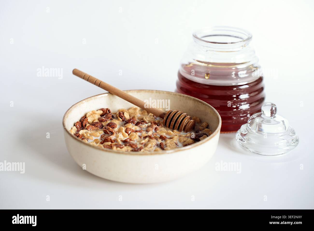 Flocons de céréales de petit déjeuner avec du lait et du miel dans un bol en céramique sur fond blanc. Banque D'Images