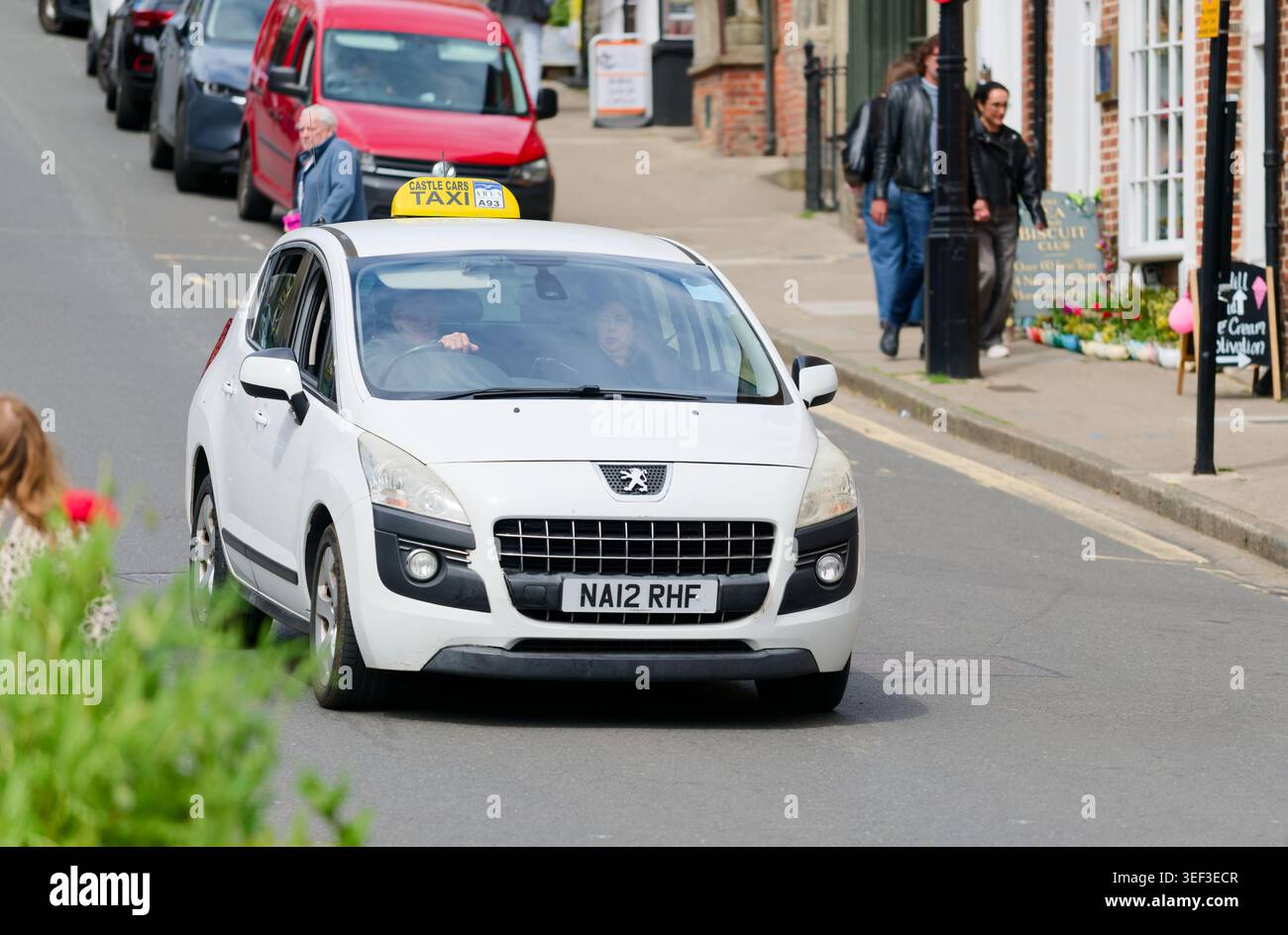 Voiture blanche Peugeot utilisée comme petit taxi, longeant une route résidentielle en Angleterre, au Royaume-Uni. Banque D'Images