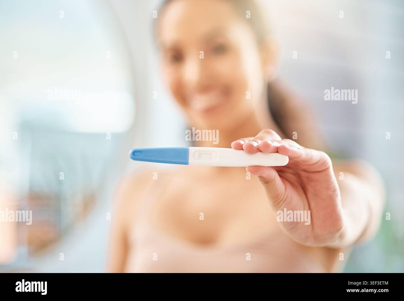 Femme heureuse, main et test de grossesse à la maison pour l'attente, la maternité ou de bonnes nouvelles dans la salle de bain. Personne féminine, sourire ou bâton de maternité avec examen Banque D'Images
