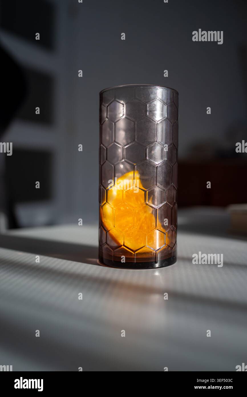 Lumière dramatique sur le coin orange, verre texturé attrapant la lueur ambre, ombres contrastées, scène de cuisine silencieuse, Banque D'Images