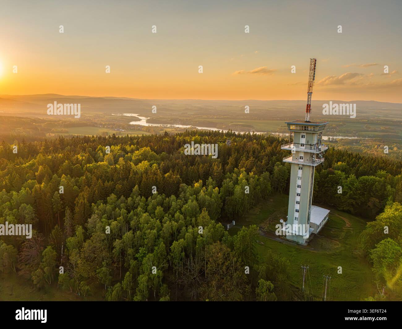 Tour de communication au-dessus de la forêt luxuriante au coucher du soleil sur la campagne vallonnée et la rivière sinueuse. Émetteur Zelena hora Banque D'Images