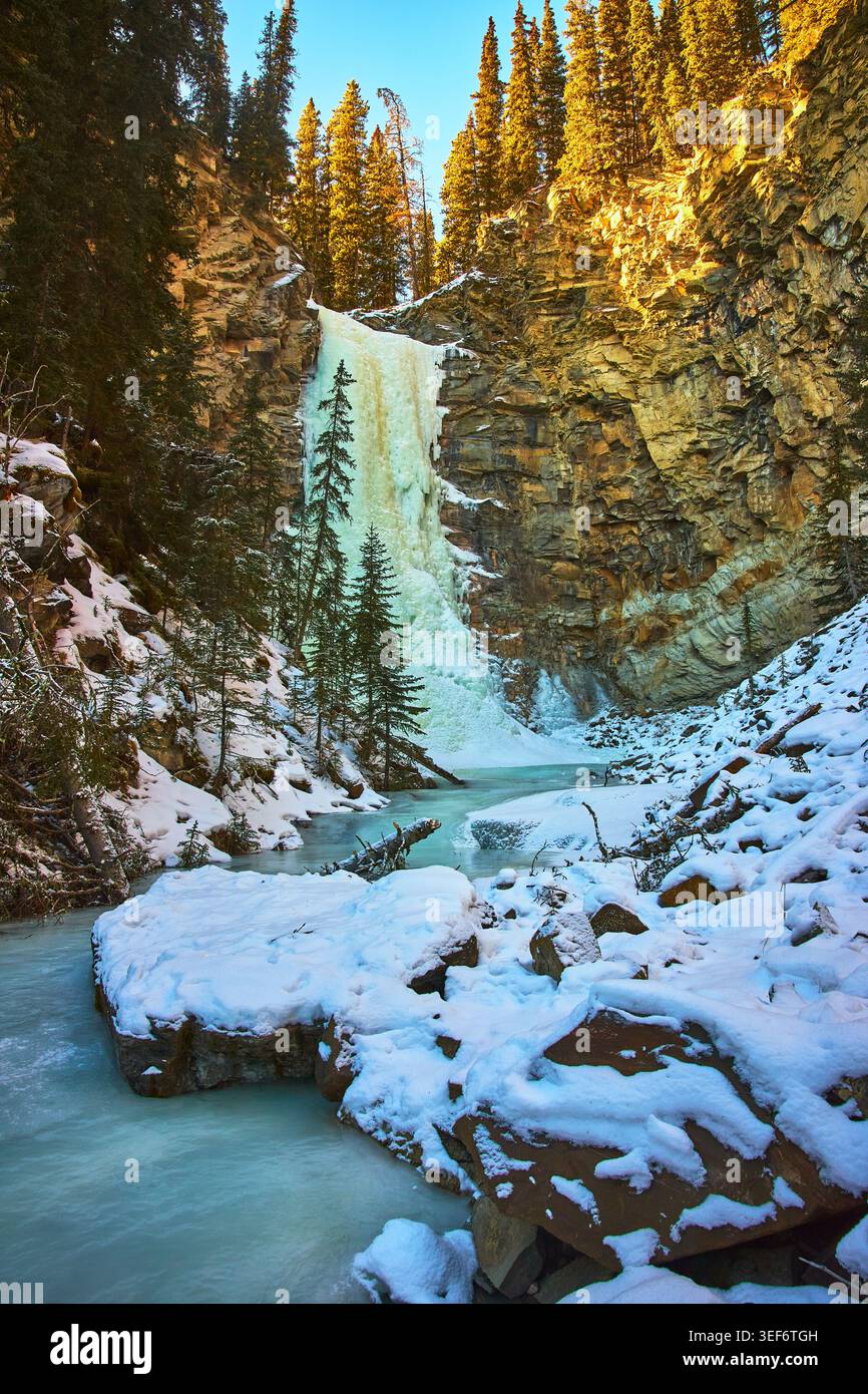 Cascade gelée et rivière dans un paysage d'hiver enneigé avec falaises et arbres Evergreen Banque D'Images
