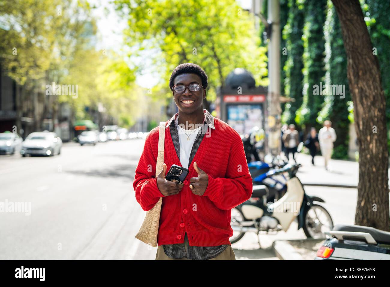 Mâle noir joyeux avec une expression positive attendant les transports en commun et souriant à la caméra. Banque D'Images
