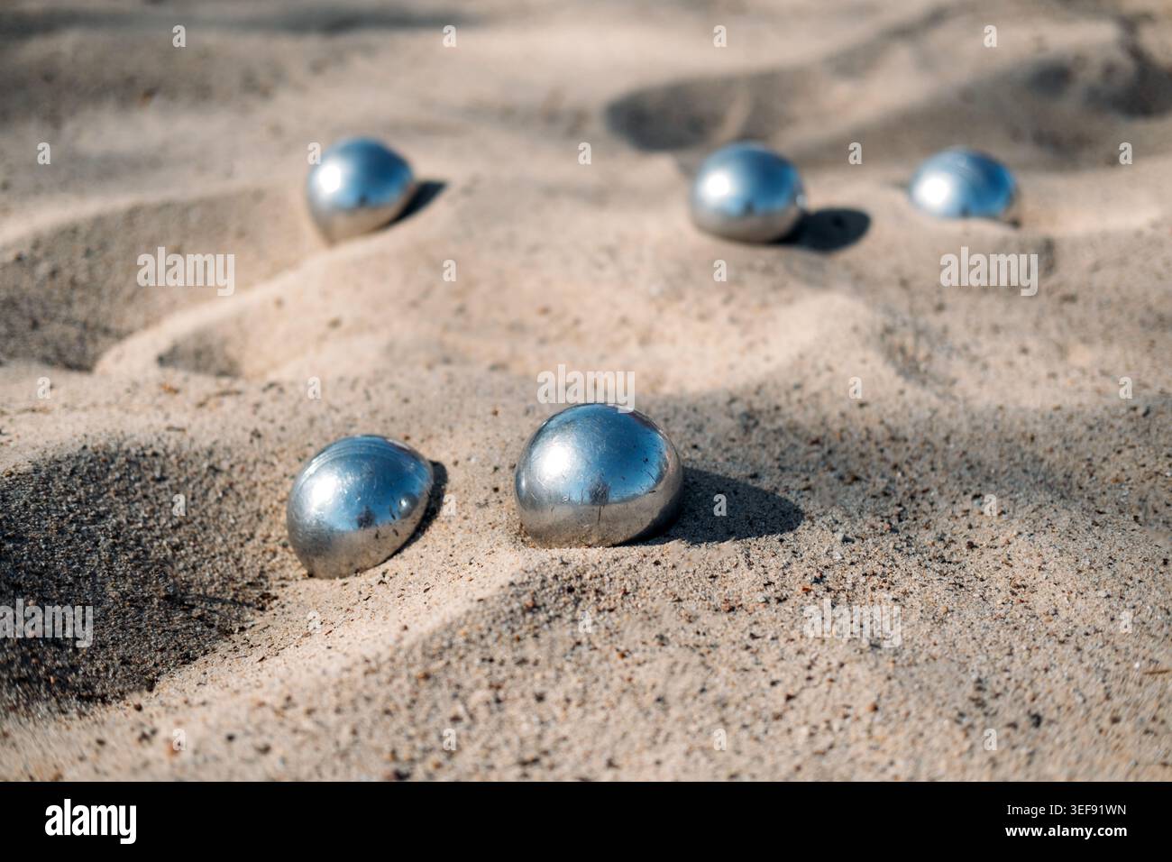 Des sphères métalliques se trouvent dispersées sur une surface sablonneuse à la lumière du soleil. Boules de pétanque, activités de la station balnéaire, animations de vacances d'été, vacances en famille Banque D'Images