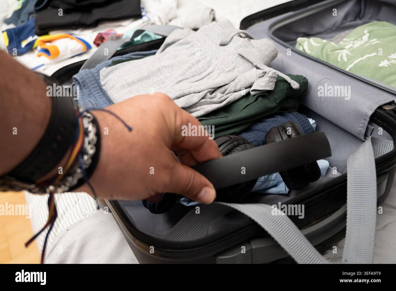 Personne emballant des écouteurs noirs dans une valise ouverte pleine de vêtements pour un voyage à venir Banque D'Images