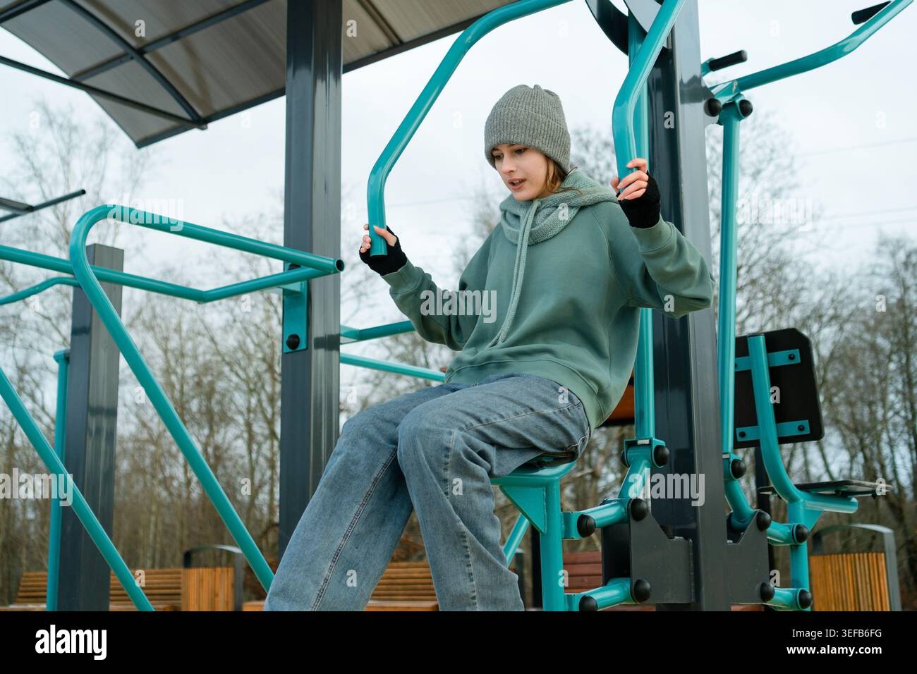 Une femme faisant des exercices de presse de bras sur l'équipement de gymnastique extérieur, regardant de côté. Routine quotidienne de maintien de la santé physique et de l'activité, mettant l'accent sur la force et l'endurance. Banque D'Images