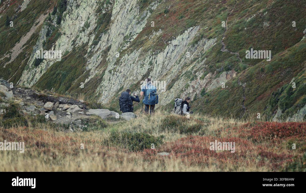 Refuge de Bellachat, France - 20.09.2025 : un groupe de trois routards trekking à travers un paysage vibrant d'arbustes alpins rouges et or sur un m escarpé Banque D'Images