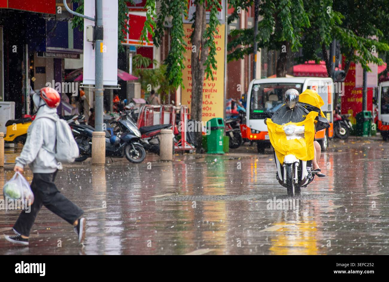 Les gens qui montent des motos portant des imperméables jaunes dans une rue pluvieuse à Ho Chi Minh-ville, Vietnam, avec des reflets sur l'asphalte humide Banque D'Images