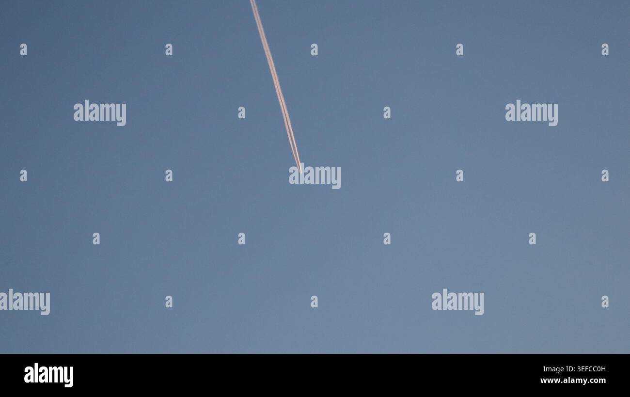 Une traînée de condensation d'avion ou une traînée de vapeur coupant à travers un ciel crépusculaire clair au crépuscule, créant une ligne graphique minimaliste. Banque D'Images