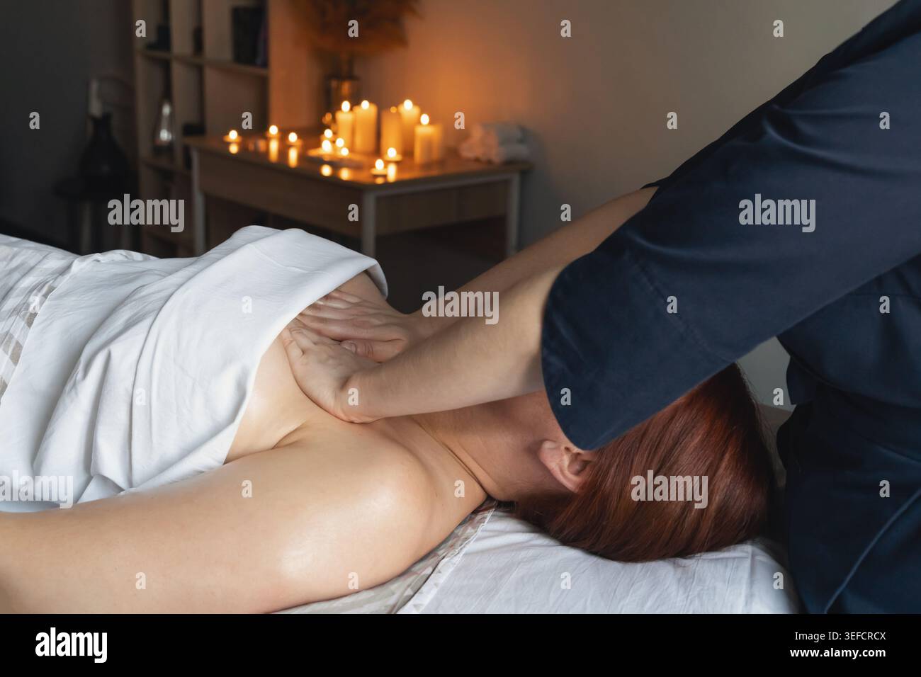 Femme allongée sur une table de massage recevant un massage professionnel du dos et des épaules dans un environnement de spa relaxant avec des bougies Banque D'Images