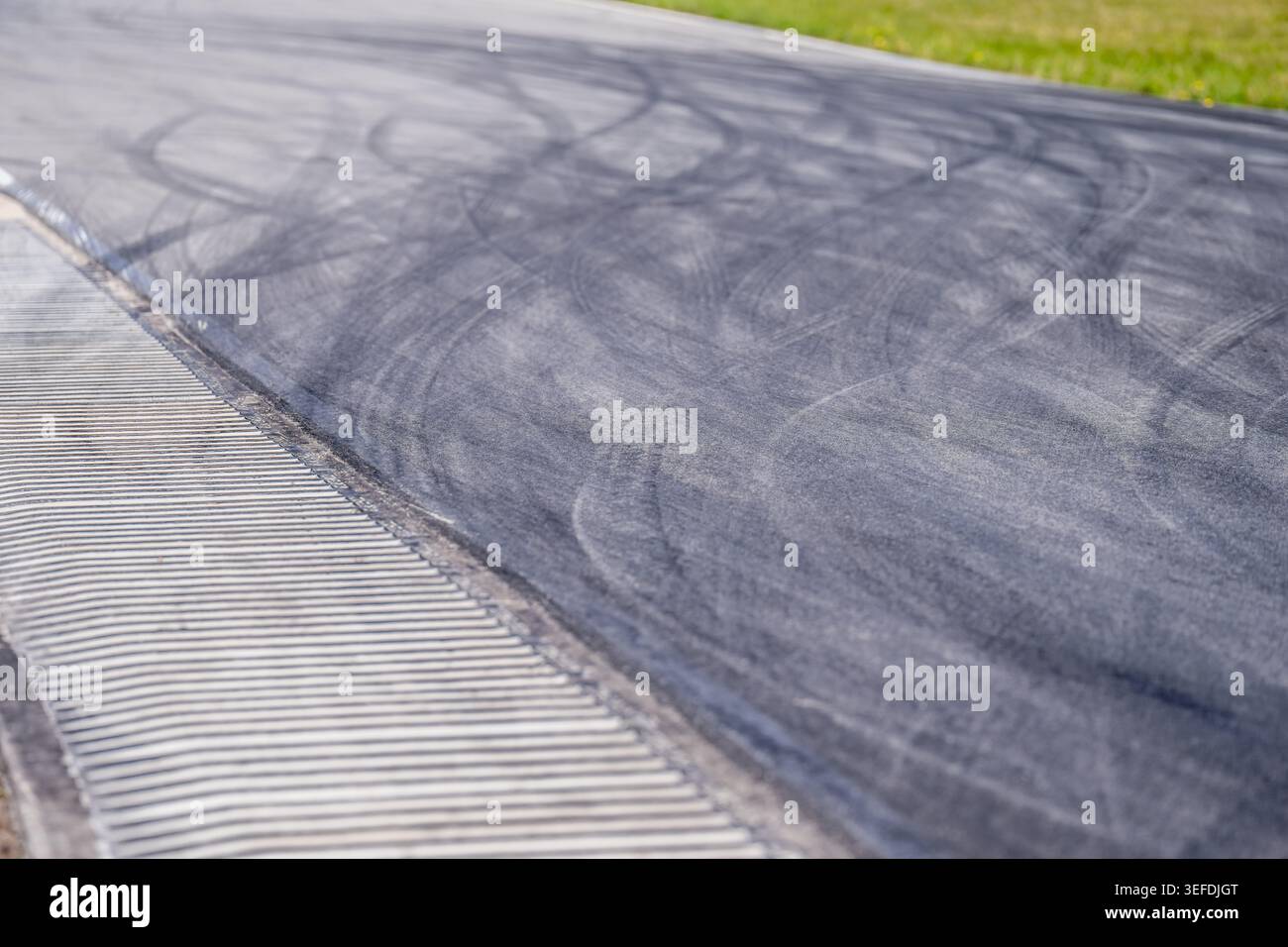 Vue en angle élevé des marques de dérapage de pneu en caoutchouc noir sur la piste de course asphaltée avec bande de grondement rayée blanche et fond d'herbe verte pour automobile spor Banque D'Images