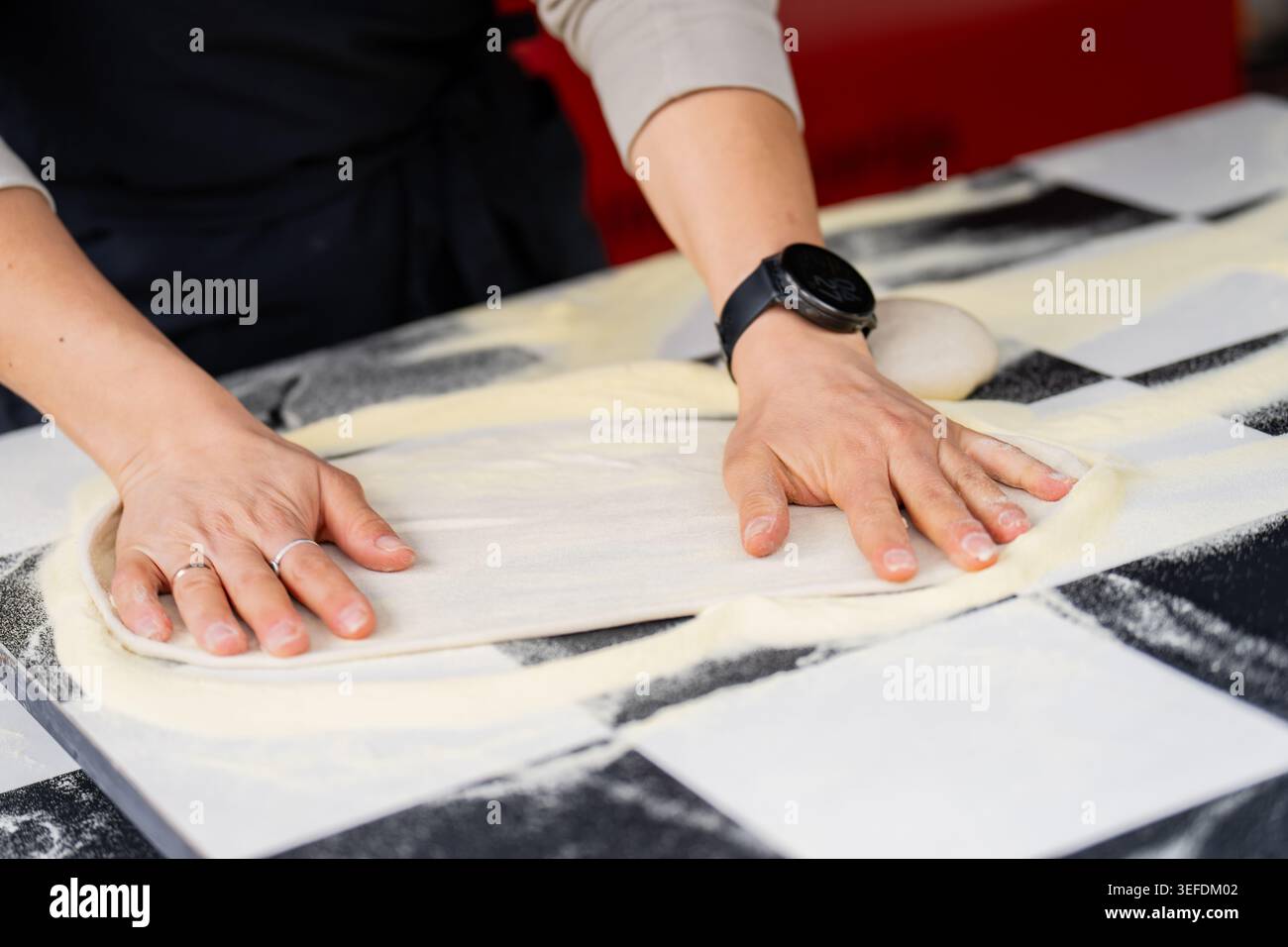 Processus manuel de façonnage de la pâte pour pizza de style italien sur un comptoir noir et blanc, illustrant la production alimentaire de petite entreprise et les compétences d'expert en pâtisserie Banque D'Images