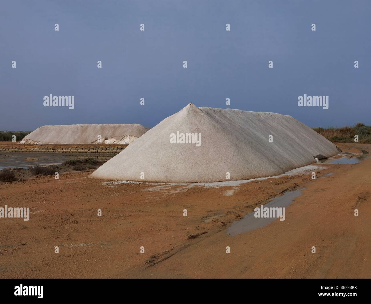 D'imposants monticules de sel de mer récolté empilés à côté des étangs d'évaporation de la saline de Trapani, en Sicile. Banque D'Images