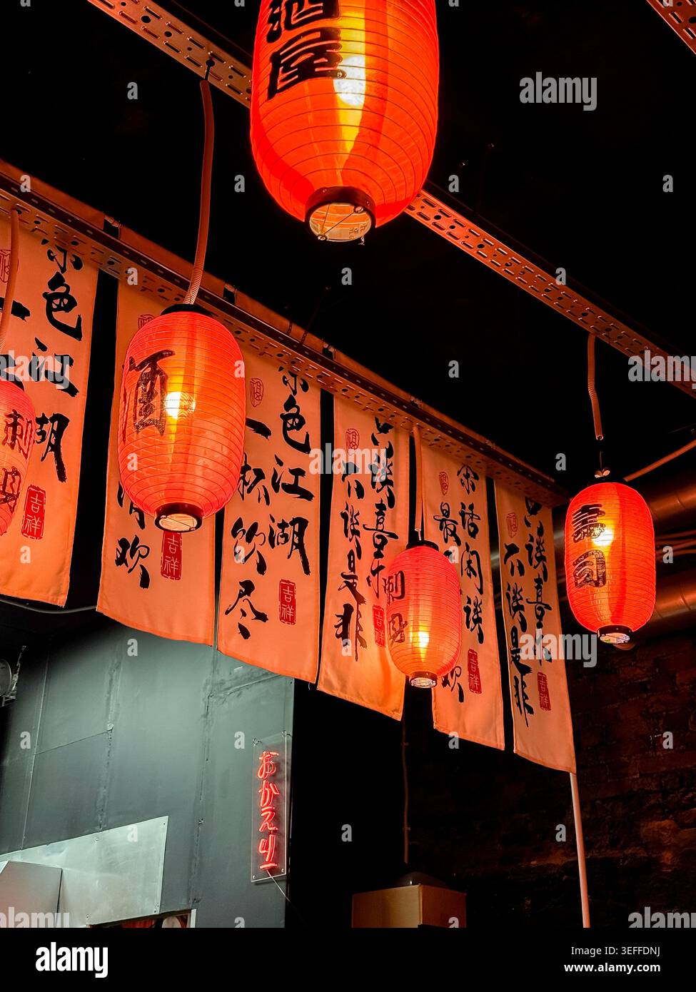 Lanternes rouges japonaises traditionnelles et bannières calligraphiques décoratives à l'intérieur d'un restaurant japonais avec un éclairage ambiant chaleureux Banque D'Images