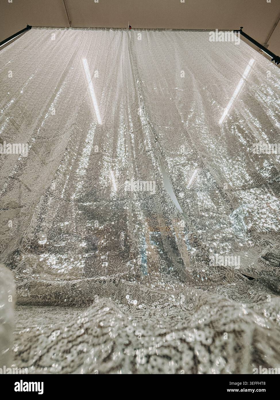 Textile à paillettes en argent étincelant suspendu dans un studio de mode ou un entrepôt de tissu. Texture glamour chatoyante avec détails réfléchissants, idéal pour le luxe Banque D'Images