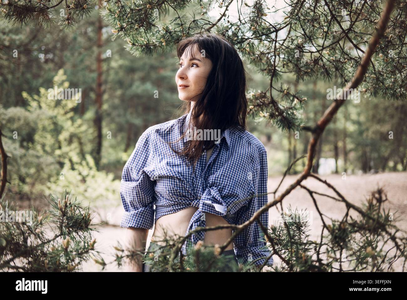 Portrait d'une femme regardant loin tout en se tenant derrière des branches de pin dans la forêt. Mode de vie détox numérique, reconnexion avec l'âme, baignade de forêt Banque D'Images