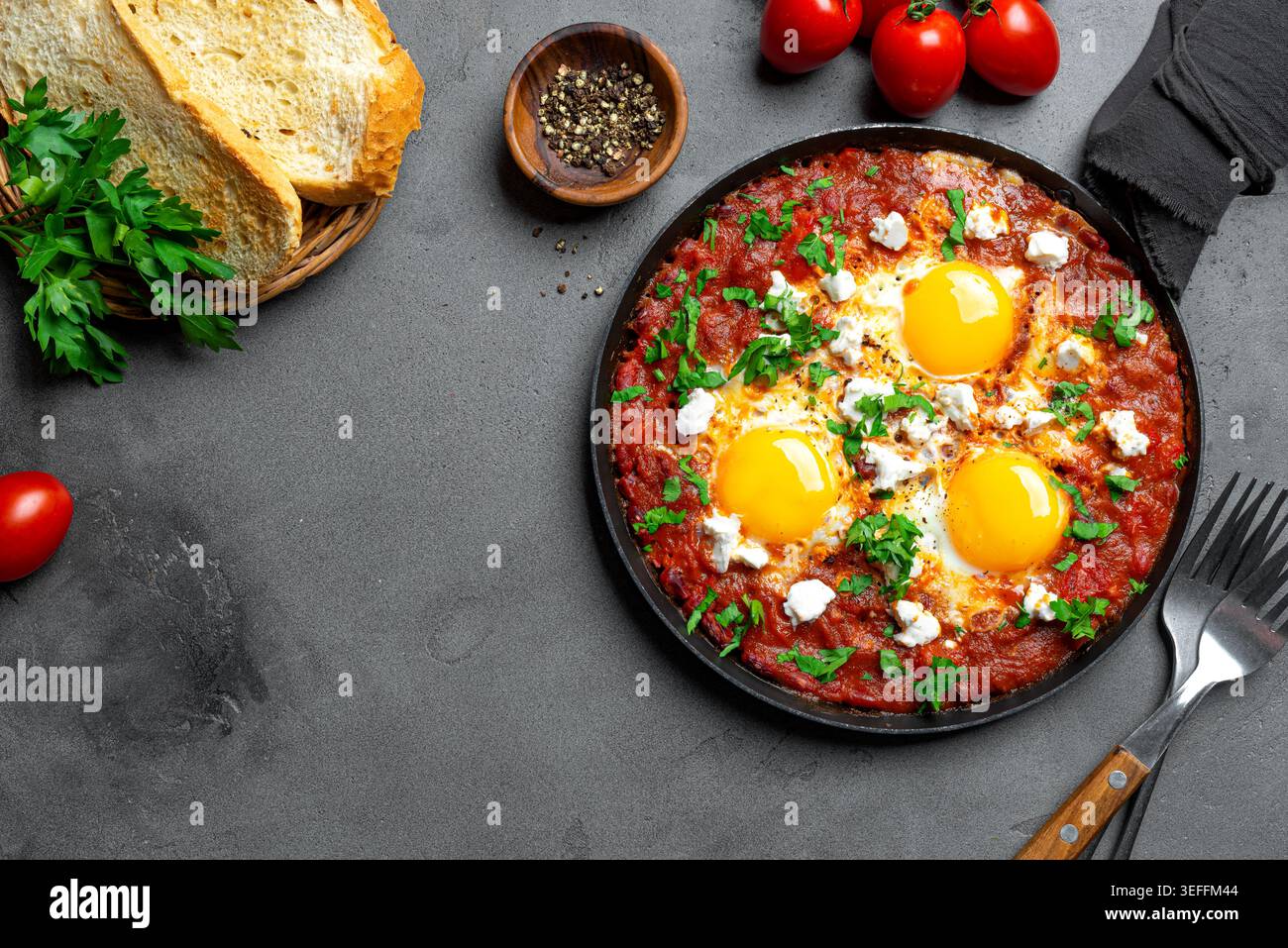 Shakshuka - oeufs frits dans une sauce tomate épicée, nappés de fromage feta et de persil dans une poêle en fonte. Shakshuka - petit-déjeuner méditerranéen Helthy sur conc Banque D'Images