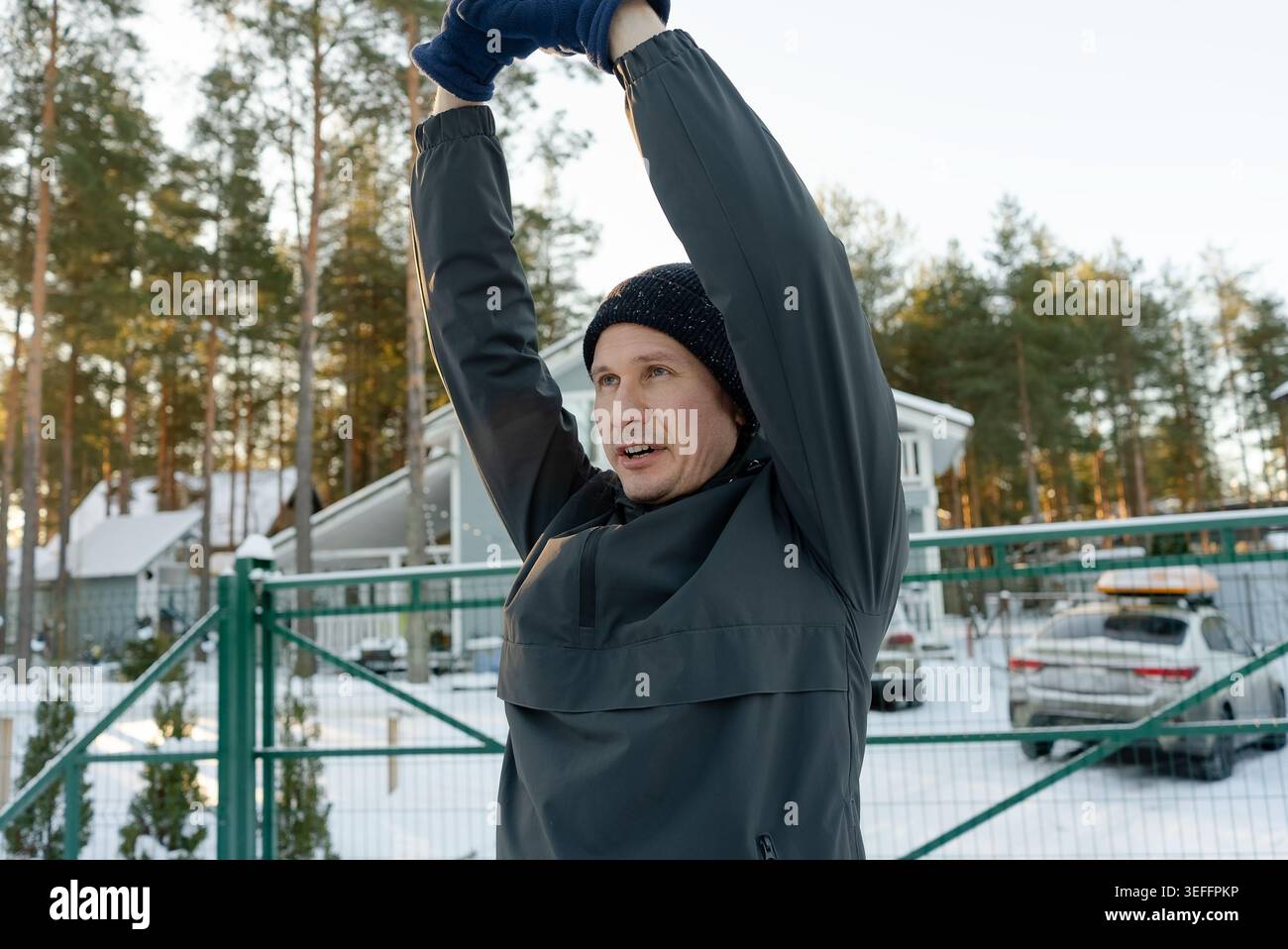Un gars dans la quarantaine lève les bras pendant une séance d'exercice en plein air. Il se réchauffe par un matin froid, en se concentrant sur la mobilité des épaules. Banque D'Images