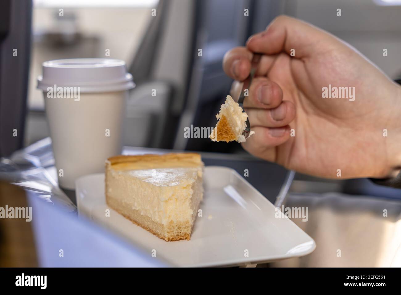 Un passager tient une fourchette avec un morceau de cheesecake à côté d'une tasse à café jetable sur un plateau d'avion, mettant en évidence le repas de voyage, les loisirs, et le c. Banque D'Images
