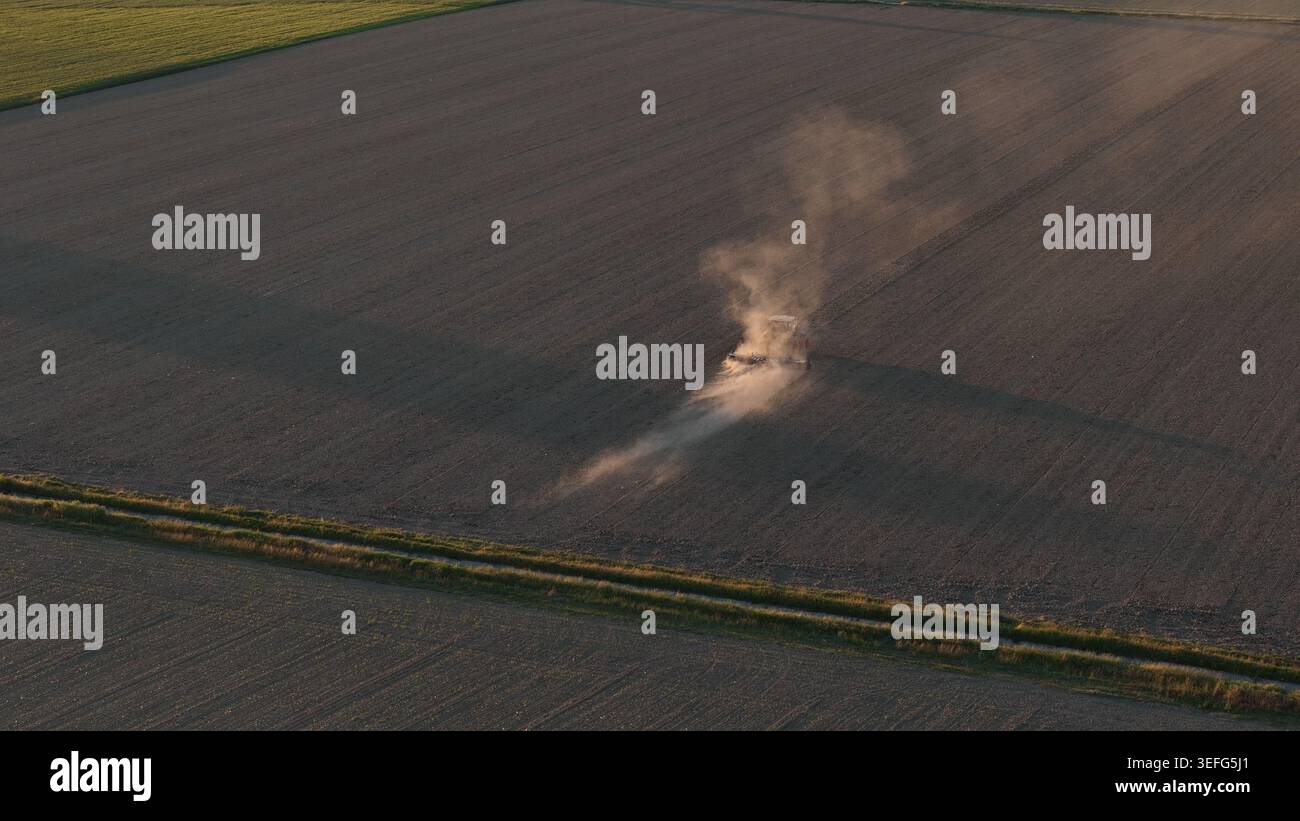 Tracteur cultivant le sol sec dans la vallée du Pô au coucher du soleil Banque D'Images