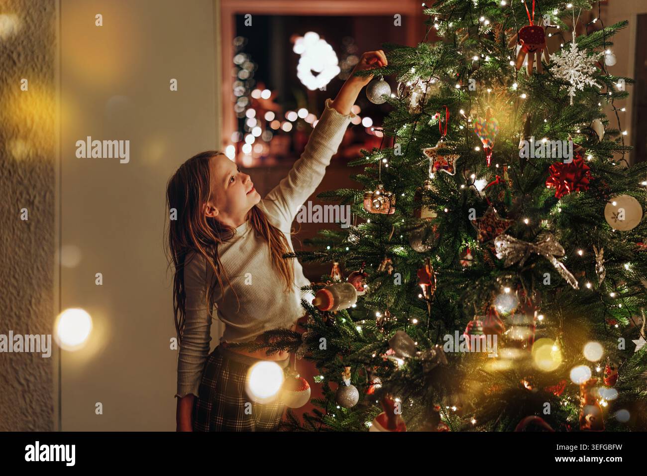 Happy Girl décore un sapin de noël. Enfants avec boule de noël. Salon décoré avec cheminée traditionnelle. Banque D'Images