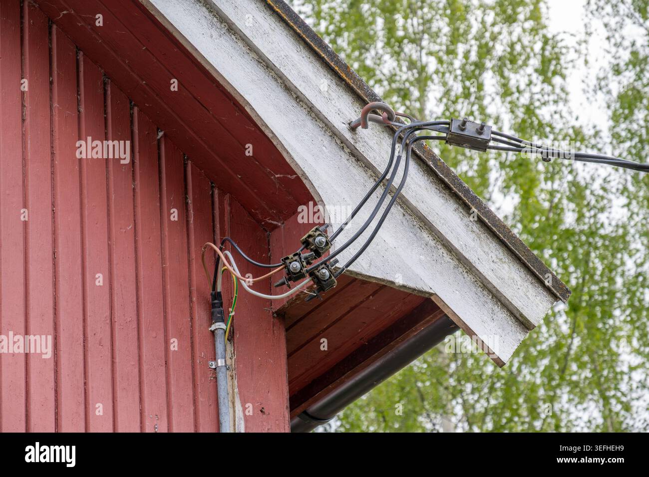 Photographie rapprochée de fils électriques exposés et de connexions de câbles montés sous le surplomb du toit d'une maison traditionnelle en bois rouge. Banque D'Images